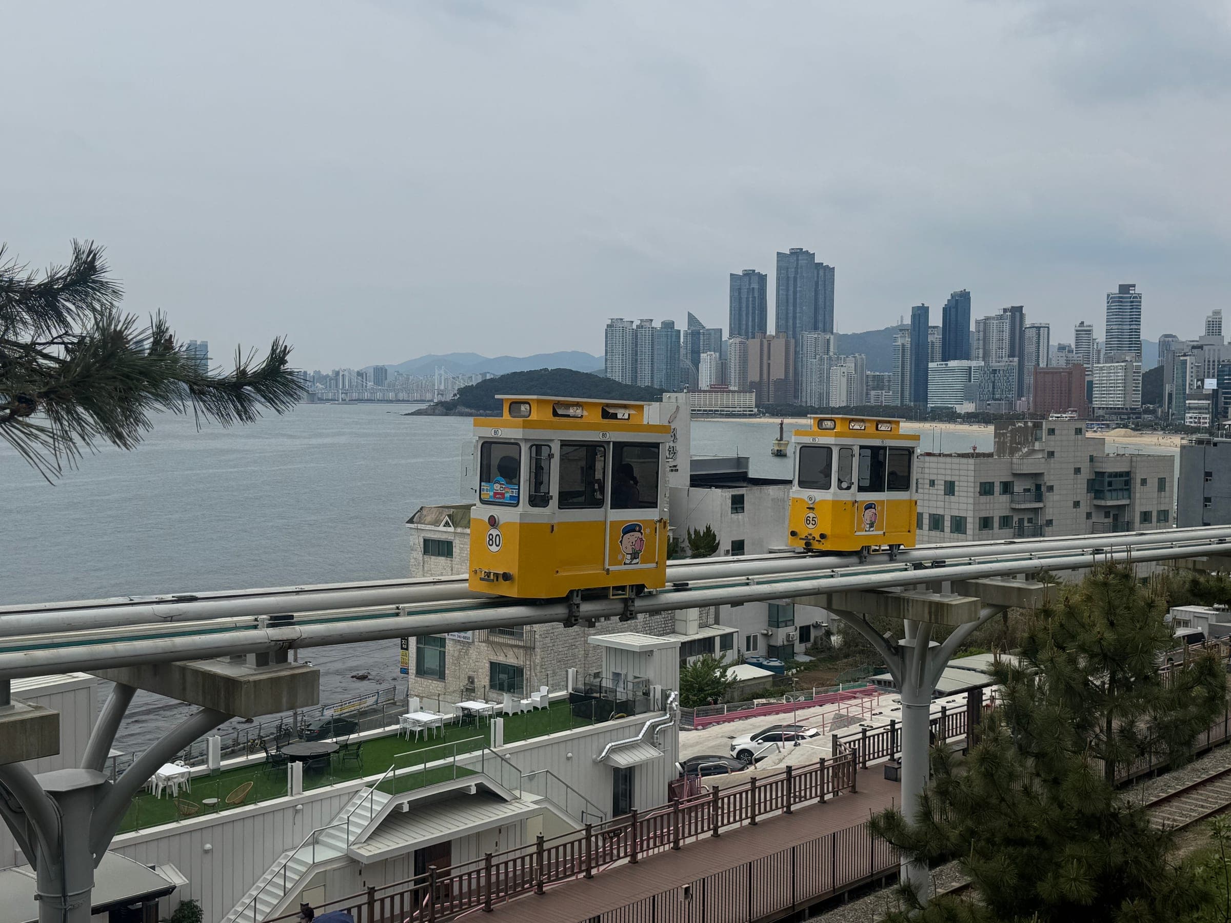 Yellow sky capsule cars on an elevated coastal track with Busan's high-rises behind