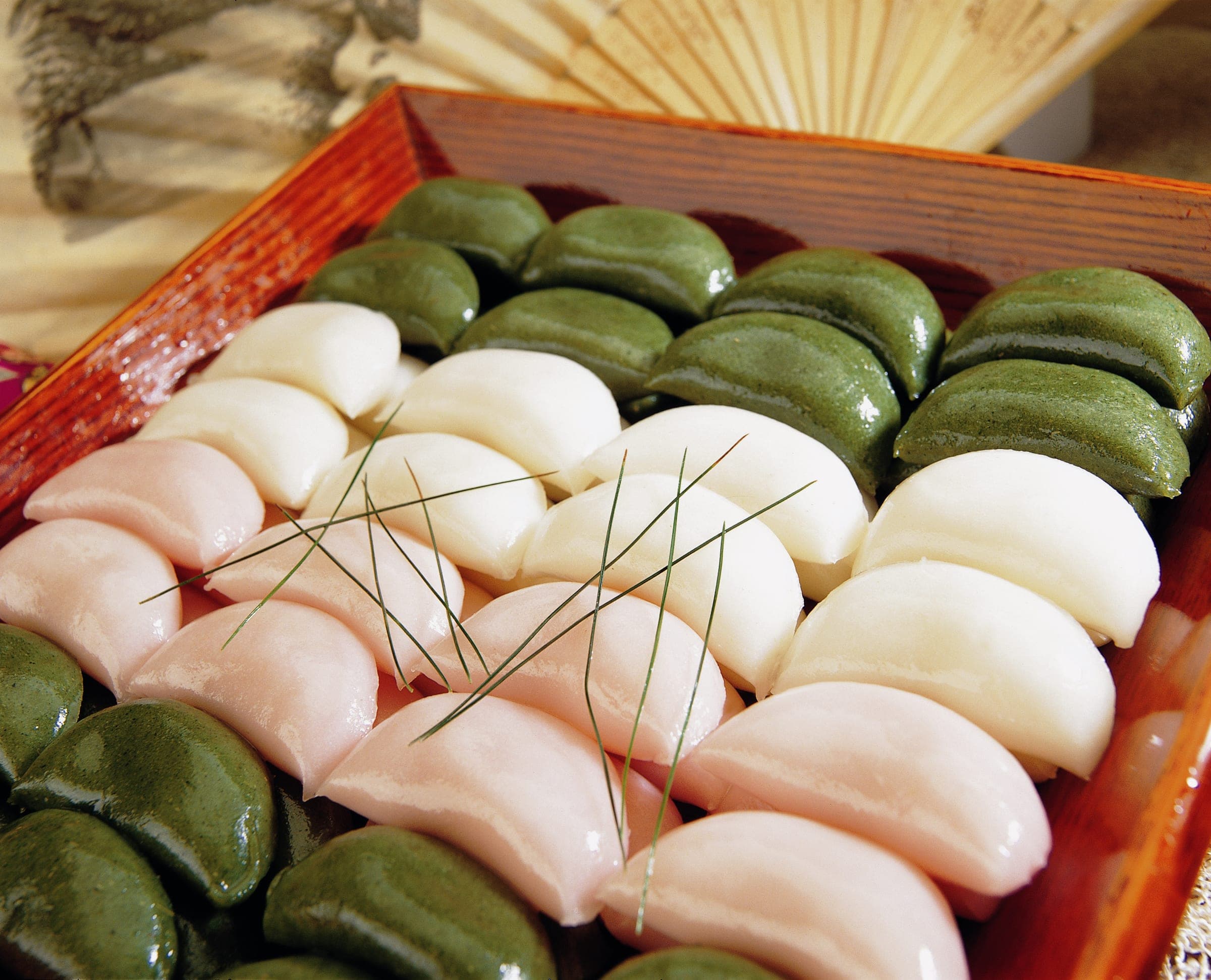 Green, white and pink songpyeon rice cakes laid out in rows on a wooden tray