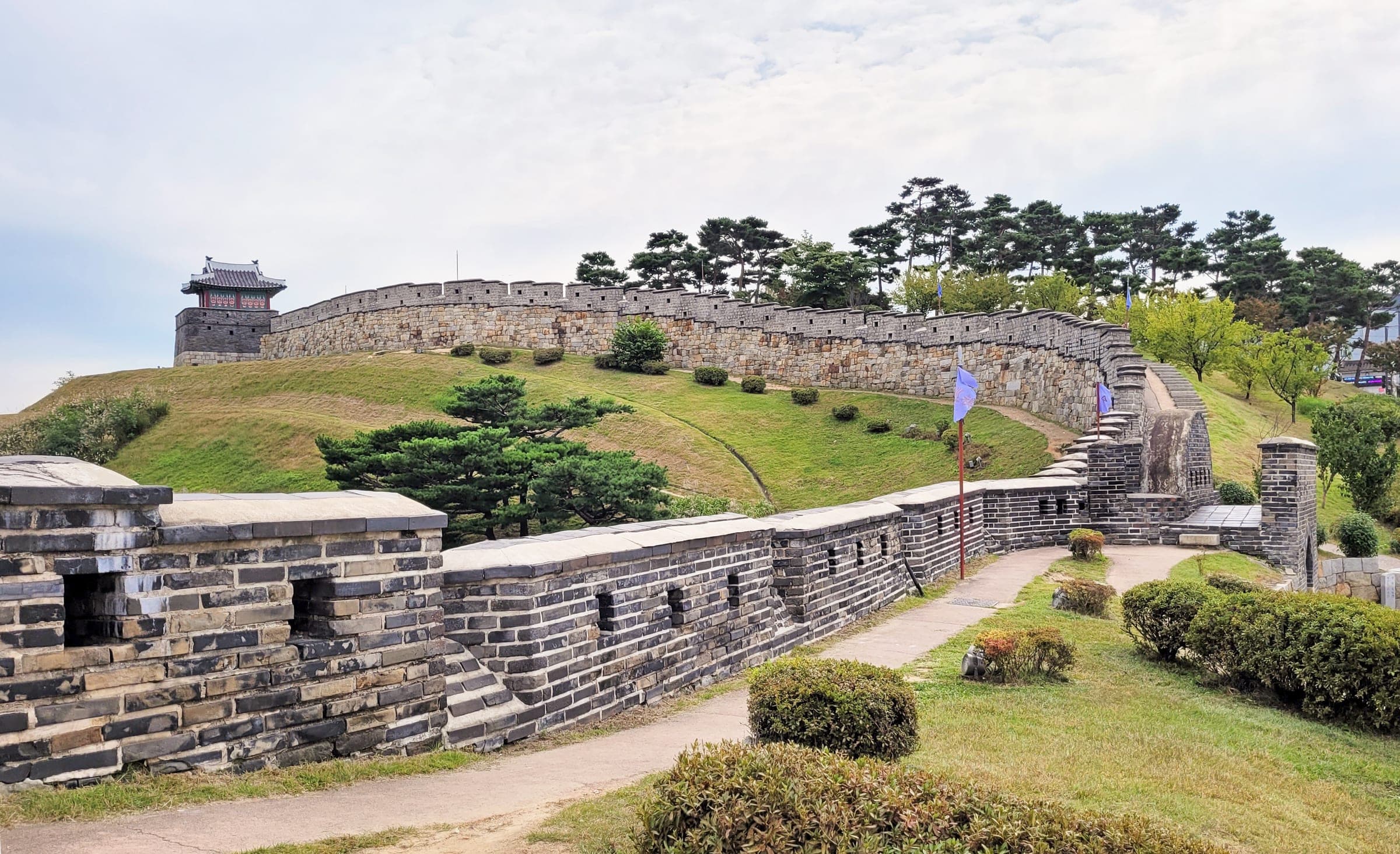 Stone walls of Hwaseong Fortress curving up a grassy slope to a watchtower in Suwon