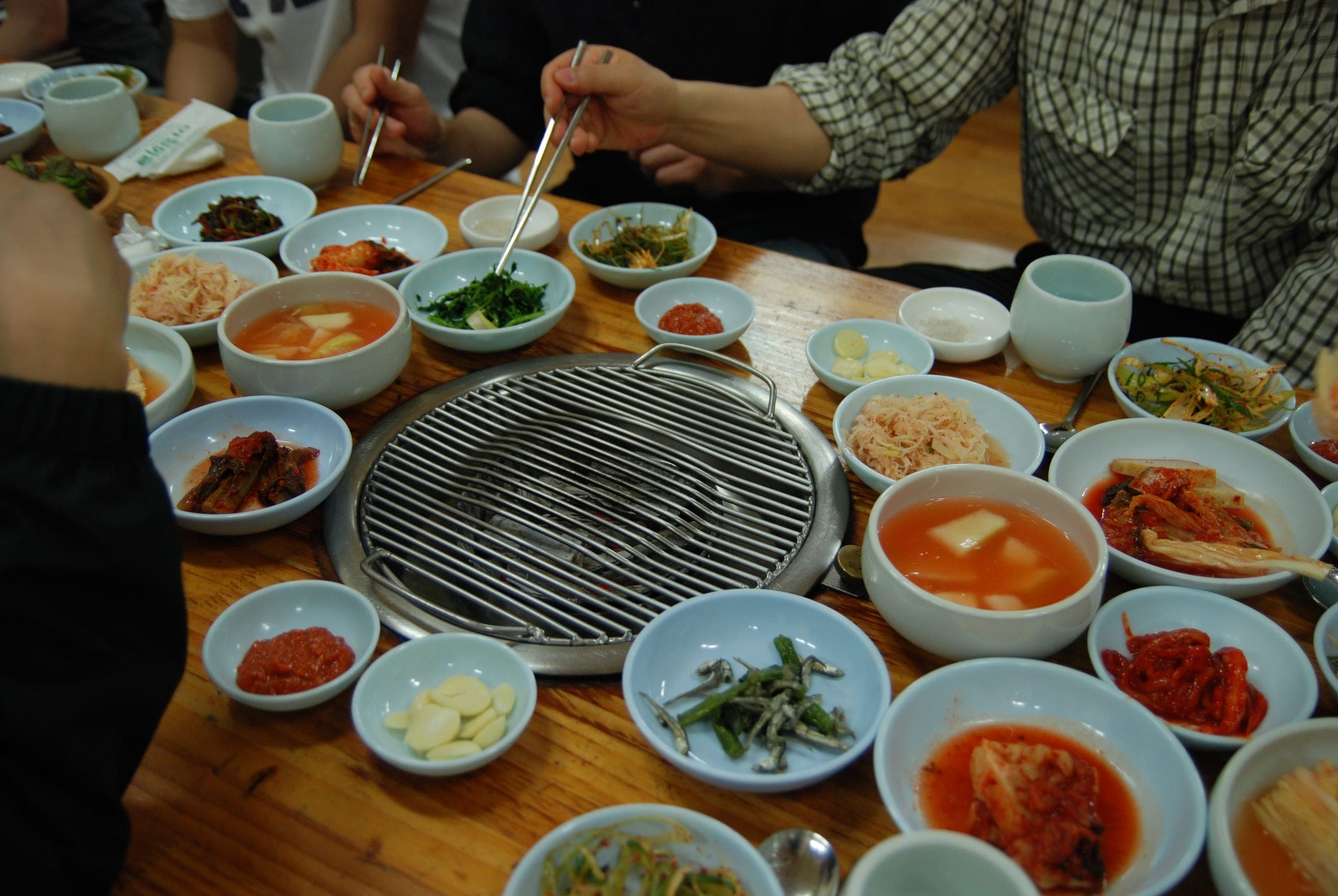 A charcoal grill set into a restaurant table, ringed by bowls of kimchi, garlic, dipping sauces and other side dishes