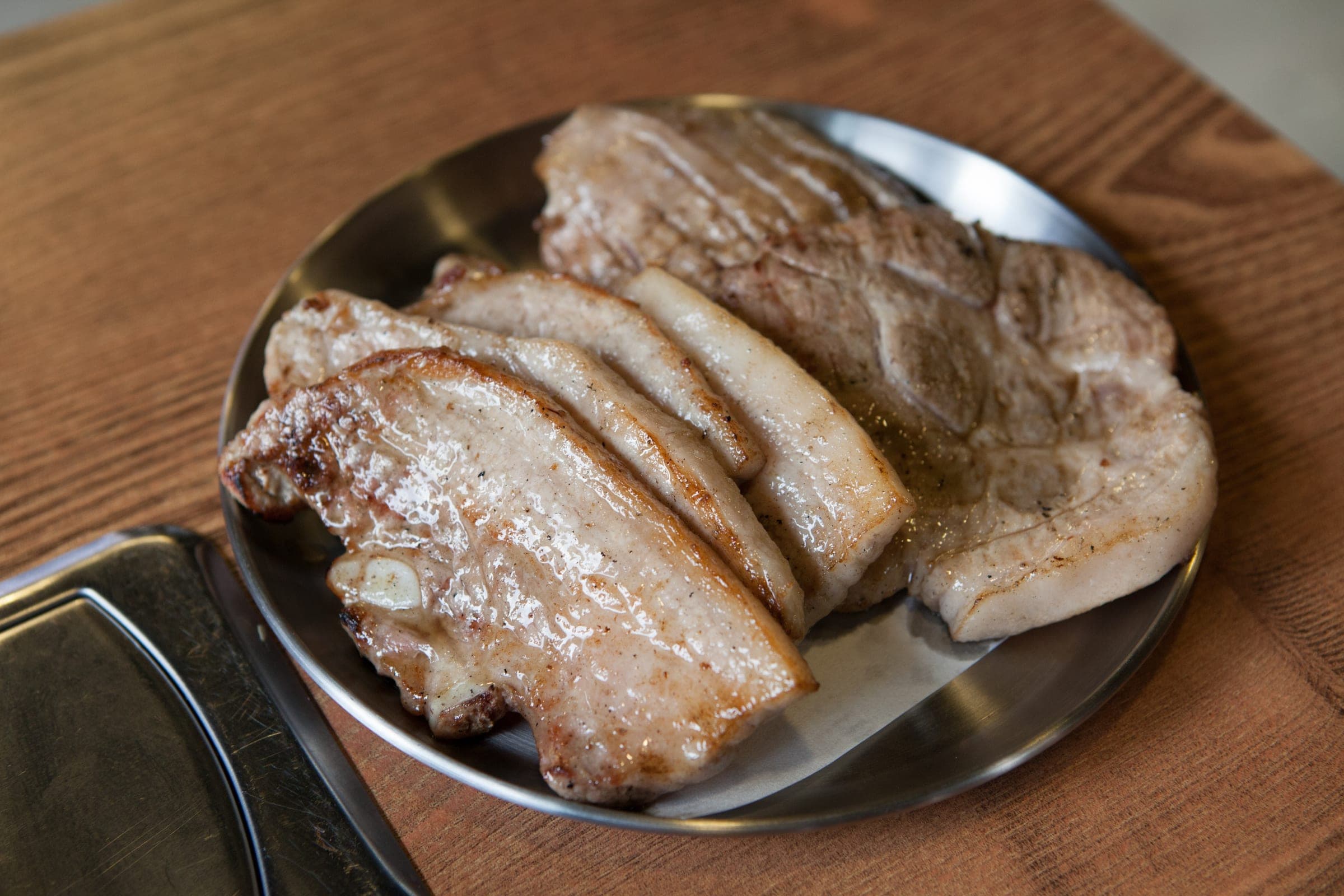 Thick slices of grilled pork on a round steel plate on a wooden table