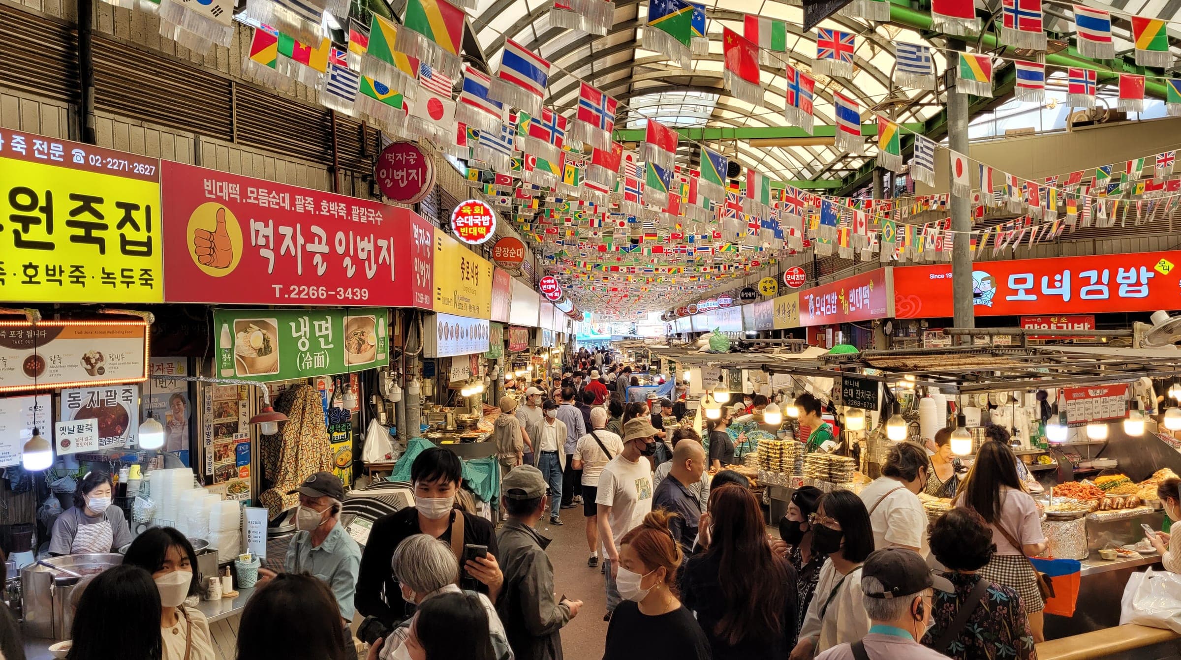 Crowded food stalls under strings of international flags inside Gwangjang Market in Seoul