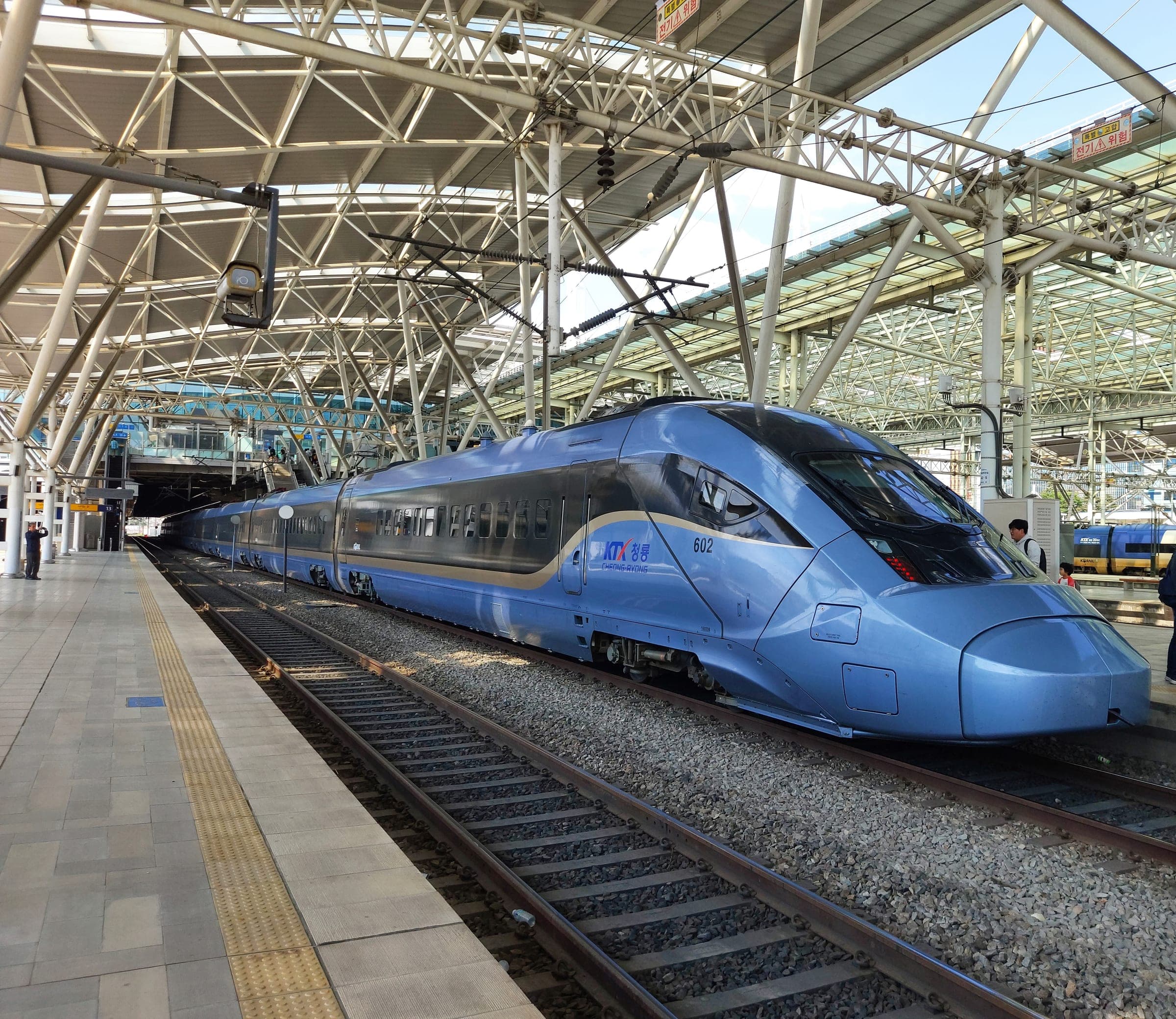 A blue KTX-Cheongryong high-speed train waiting at a platform under the steel roof of Seoul Station