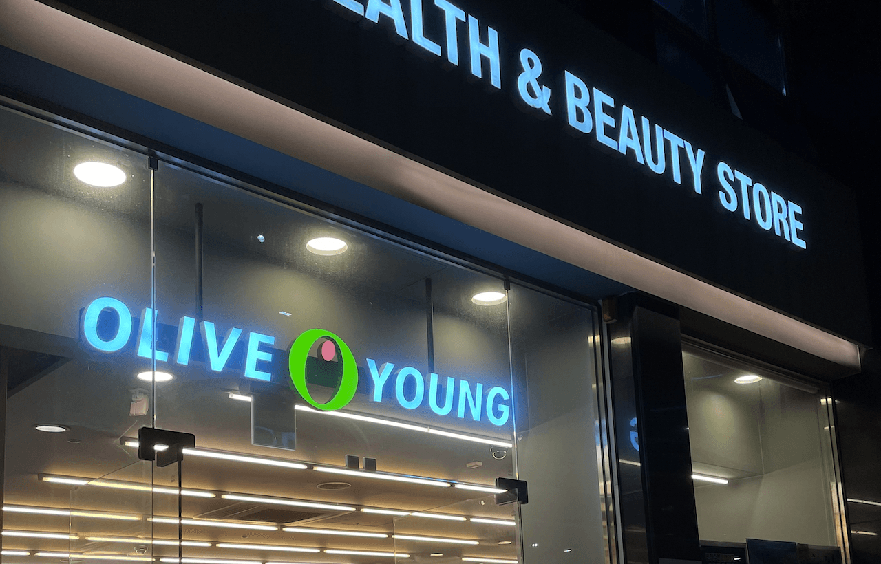 Lit Olive Young sign and Health and Beauty Store lettering over a glass shopfront at night