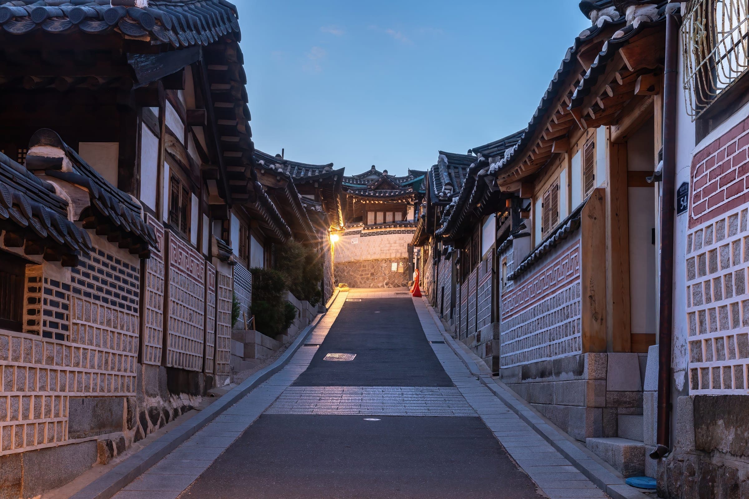 Tiled hanok rooftops lining a sloping lane in Bukchon Hanok Village at dusk