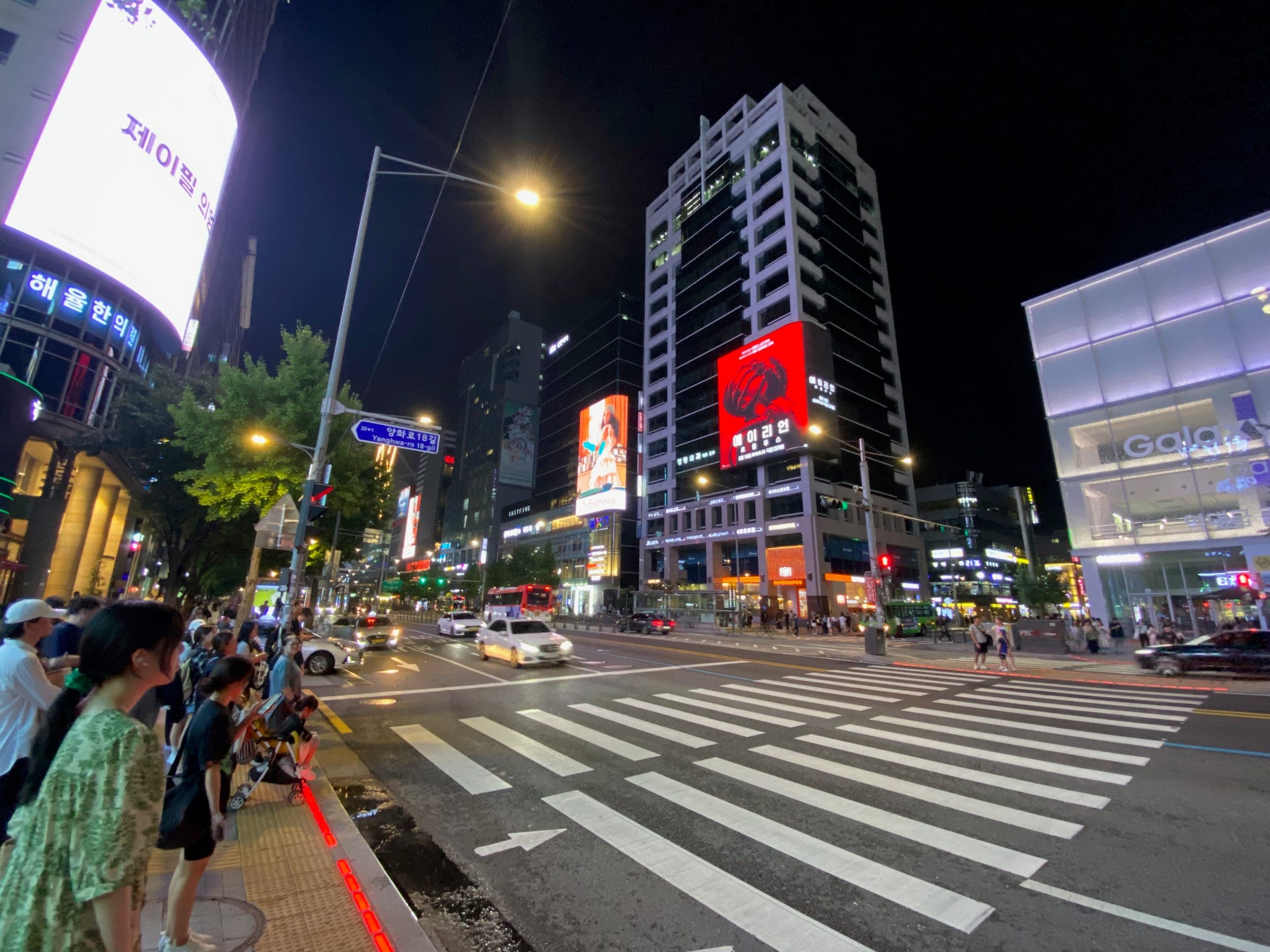 Crowds at a busy Hongdae crossing lit by billboards at night