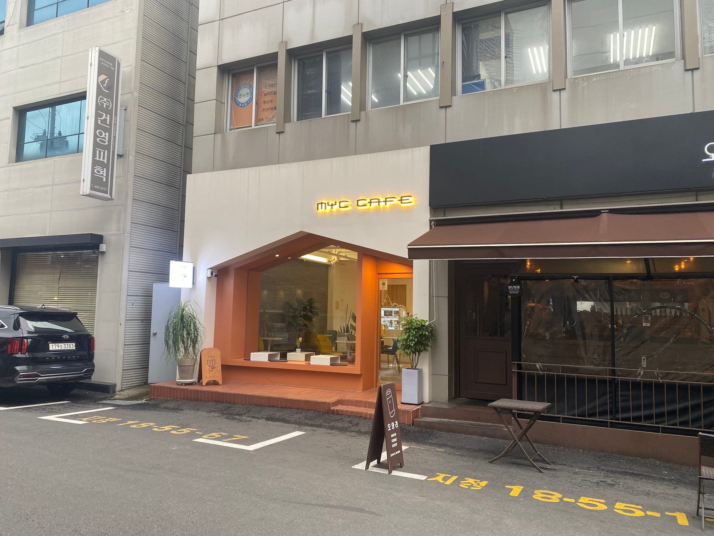 A cafe with an orange window frame next to other shopfronts on a Seongsu-dong side street