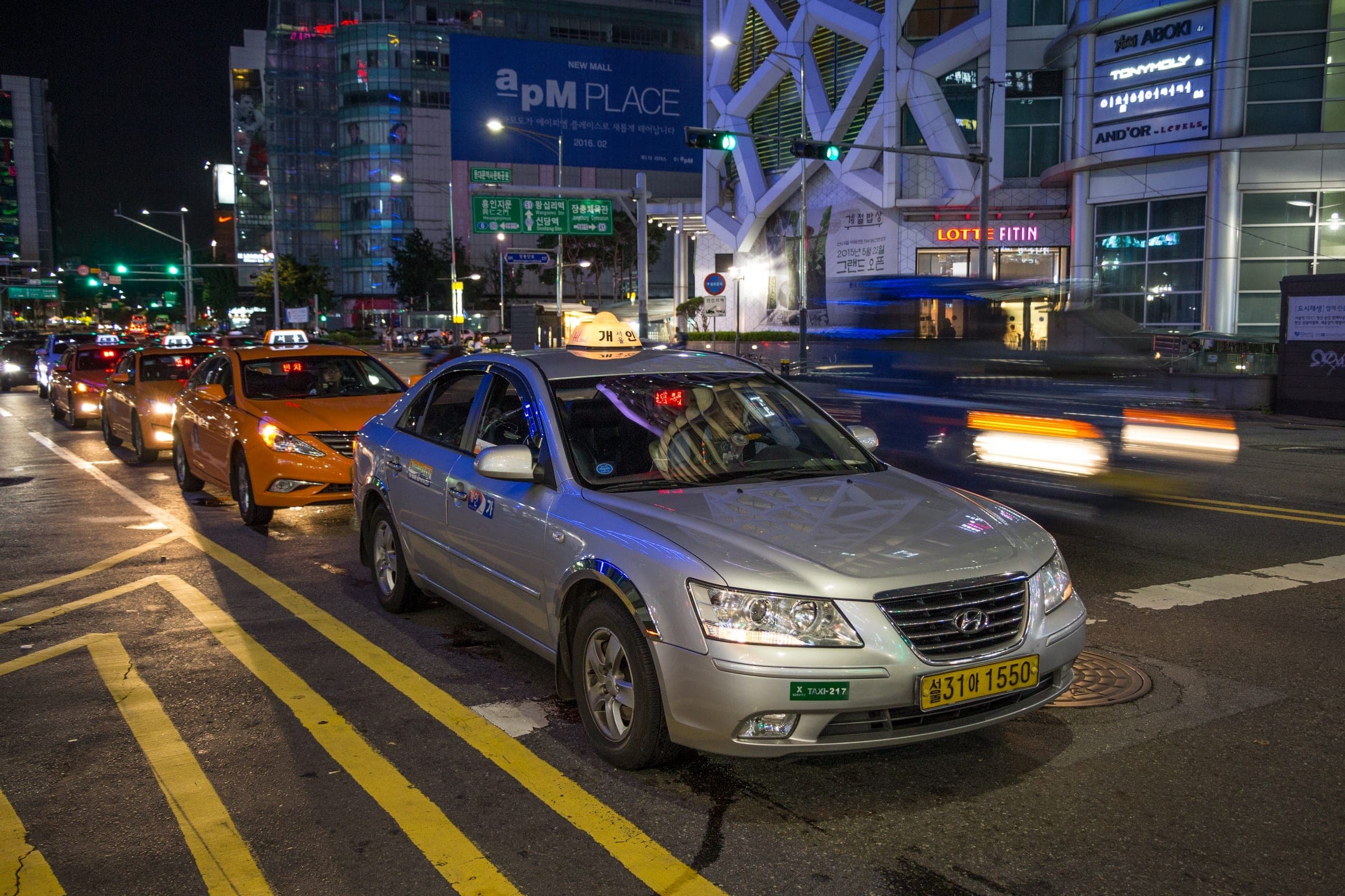 Silver and orange taxis lined up on a Seoul street at night